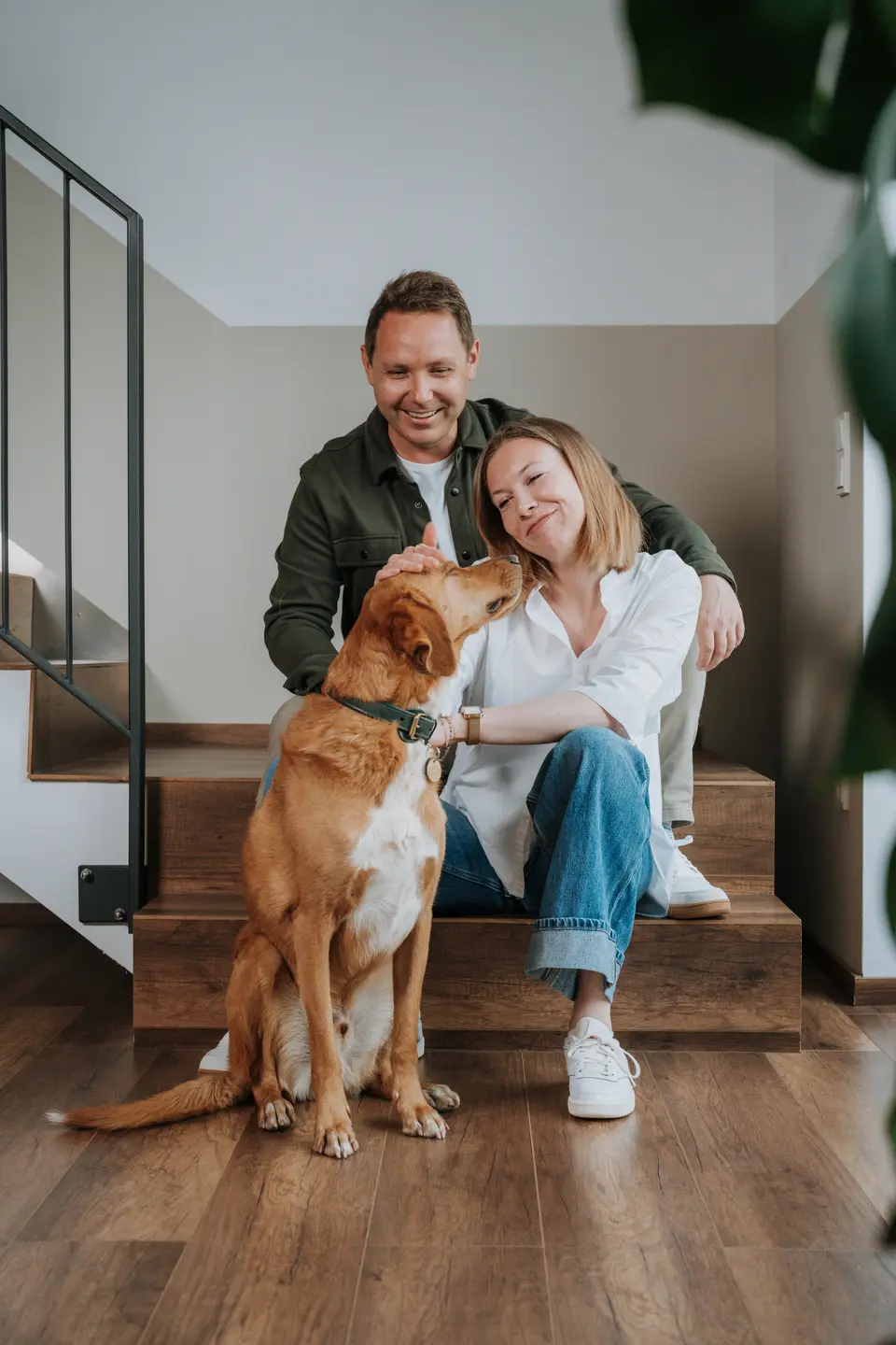 Denis Klefenz und Jill sitzen lächelnd mit ihrem goldenen Labrador auf der Treppe