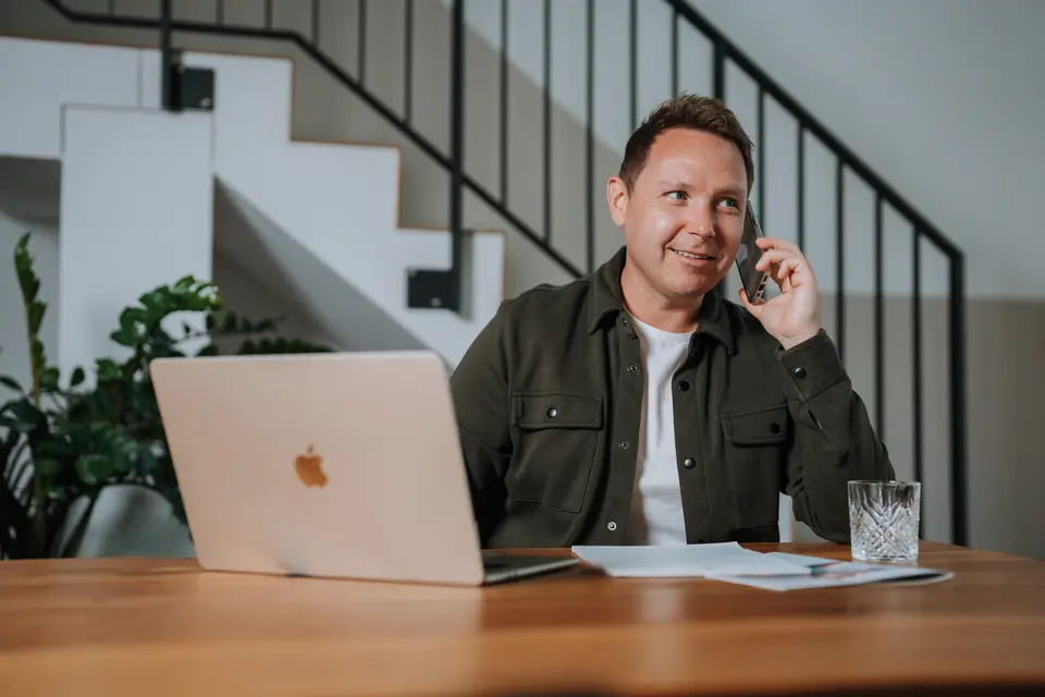 Denis Klefenz telefoniert am Holztisch mit Laptop und Unterlagen – Kontakt Versicherungsmakler Hemsbach