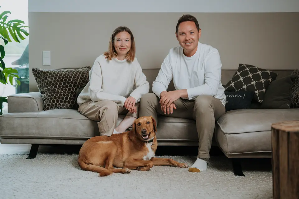 Denis Klefenz und Jil sitzen auf dem Sofa mit ihrem goldenen Labrador, der davor auf dem Teppich liegt