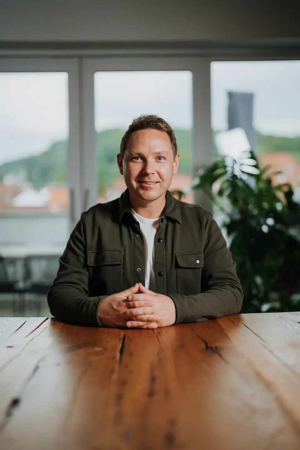 Denis Klefenz sitzt am rustikalen Holztisch mit Blick aus dem Panoramafenster auf Hemsbach