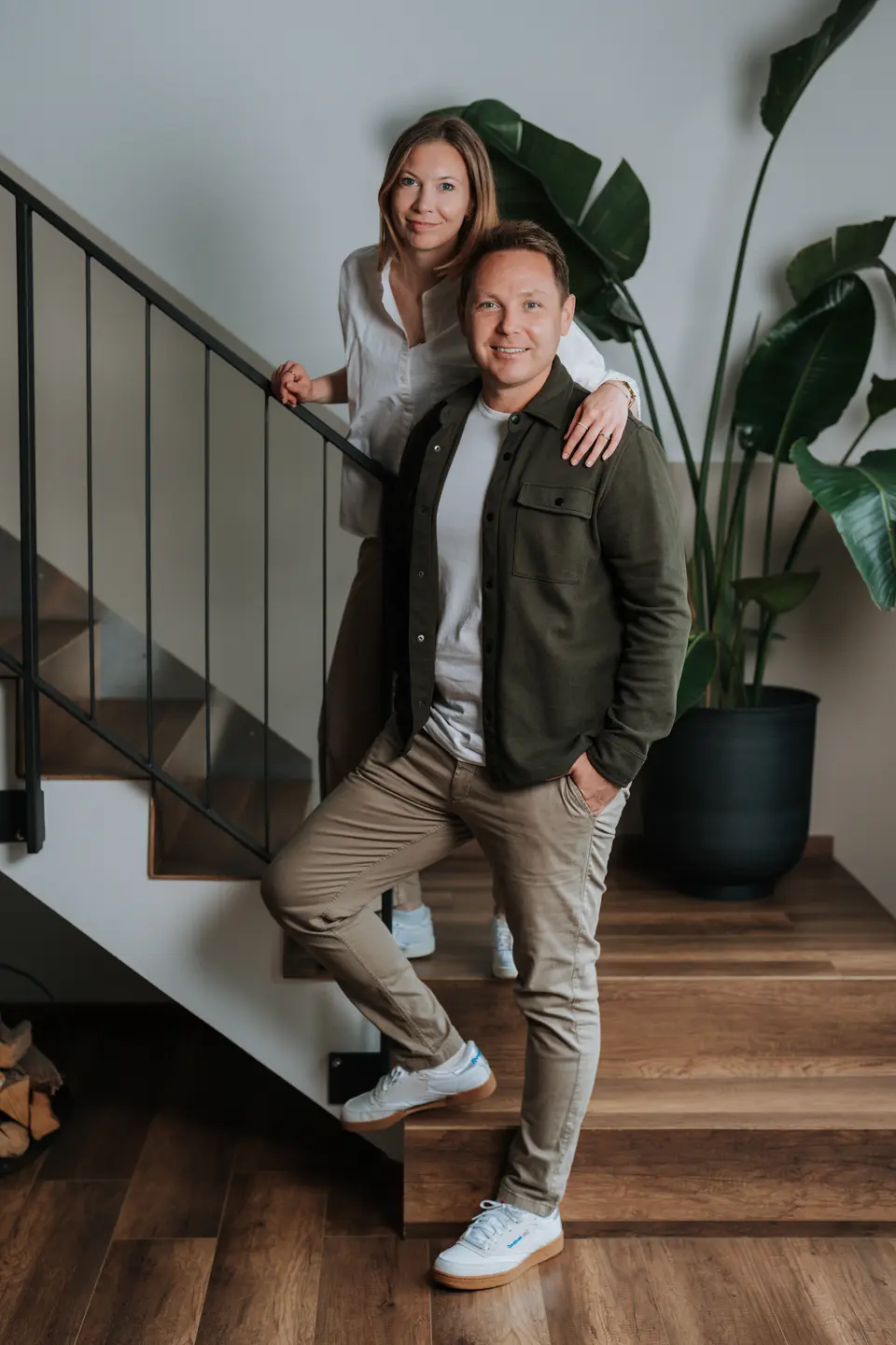 Denis Klefenz und Jil stehen lächelnd nebeneinander an einer Treppe mit großer Zimmerpflanze