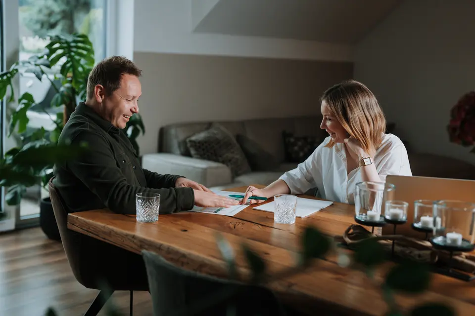 Denis Klefenz und Jil besprechen gemeinsam Unterlagen am Holztisch im Wohnzimmer